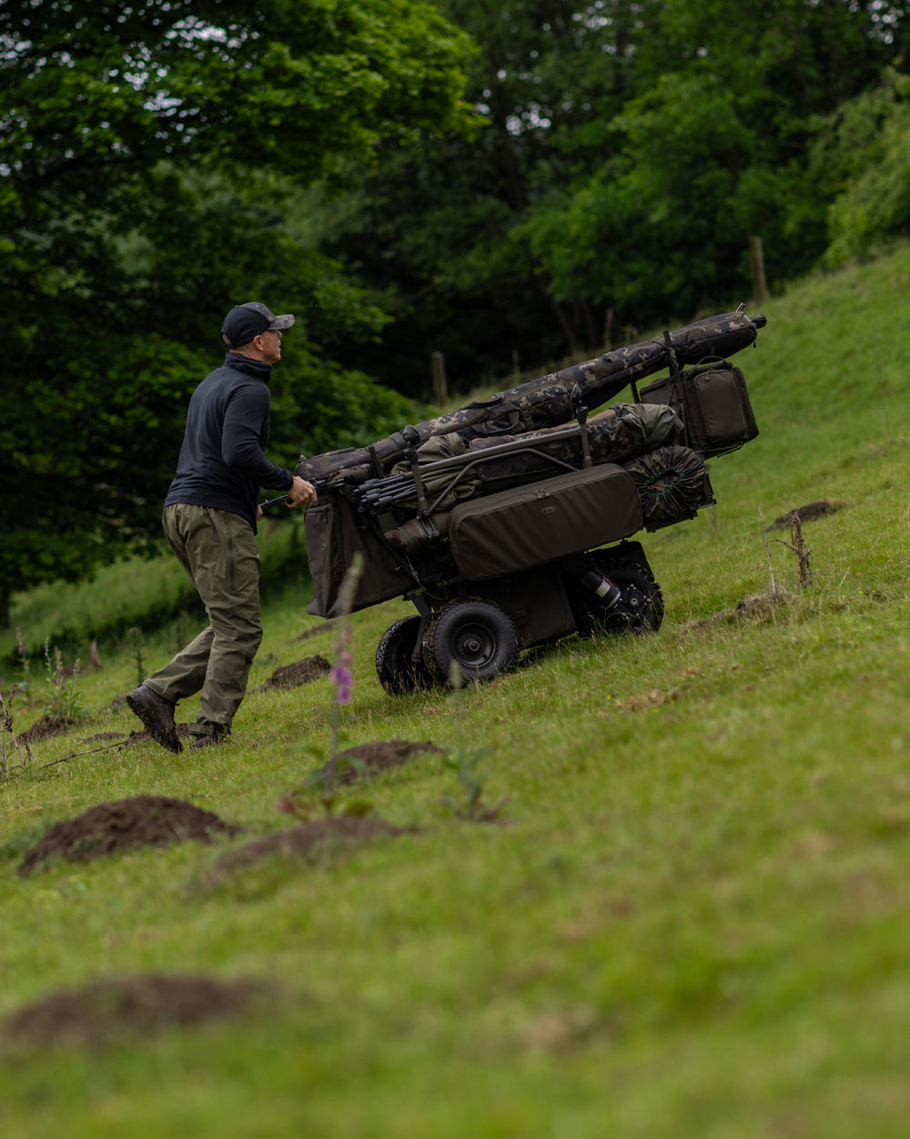 Person pushing a large hunting blind through a grassy field with trees in the background